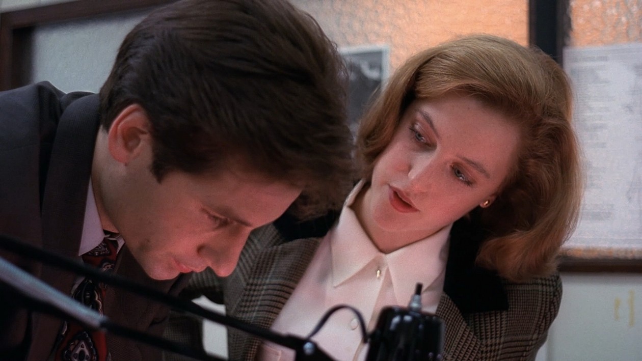 Mulder and Scully leaning over a tape deck together in the sheriff's office